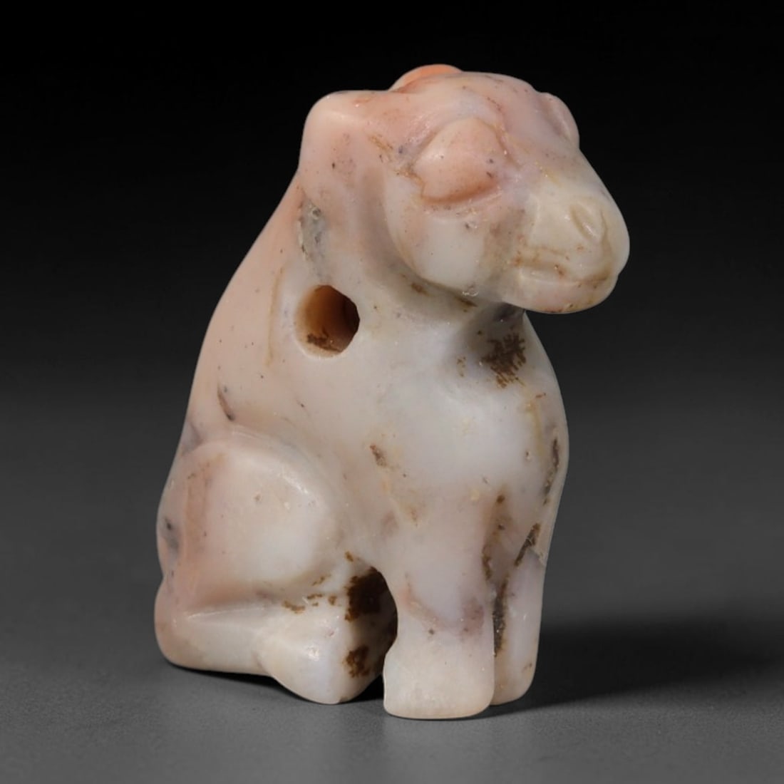 Ancient Western Asiatic Recumbent Beast Zoomorphic Amulet (1000-600 BCE), 19AB, 19AB: Hand-carved pale blush translucent hardstone pendant shaped as a seated feline figure with simplified smooth facial contours and rounded eye detailing. A clean perforated suspension hole is drilled th