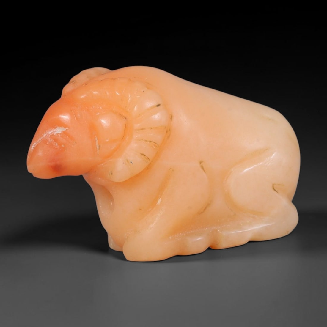 Ancient Sasanian Persian Natural Peach Calcite Recumbent Ram Amulet (224-651 CE), 32AB, 32AB: Smoothly carved pale peach calcite recumbent ram talisman, featuring neatly incised curved detailing on spiral horns to delineate texture. The stone holds a soft ancient polish with faint natural mine