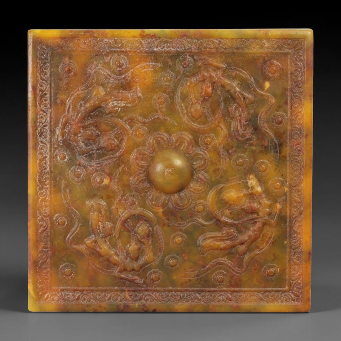 A Chinese Jade Relief Plaque, 20th Century, 50FD, 50FD: Carved from mottled yellow-brown and olive-toned jade with areas of natural translucency and darker inclusions. The plaque is square in form and worked in shallow to moderate relief on one face, frame