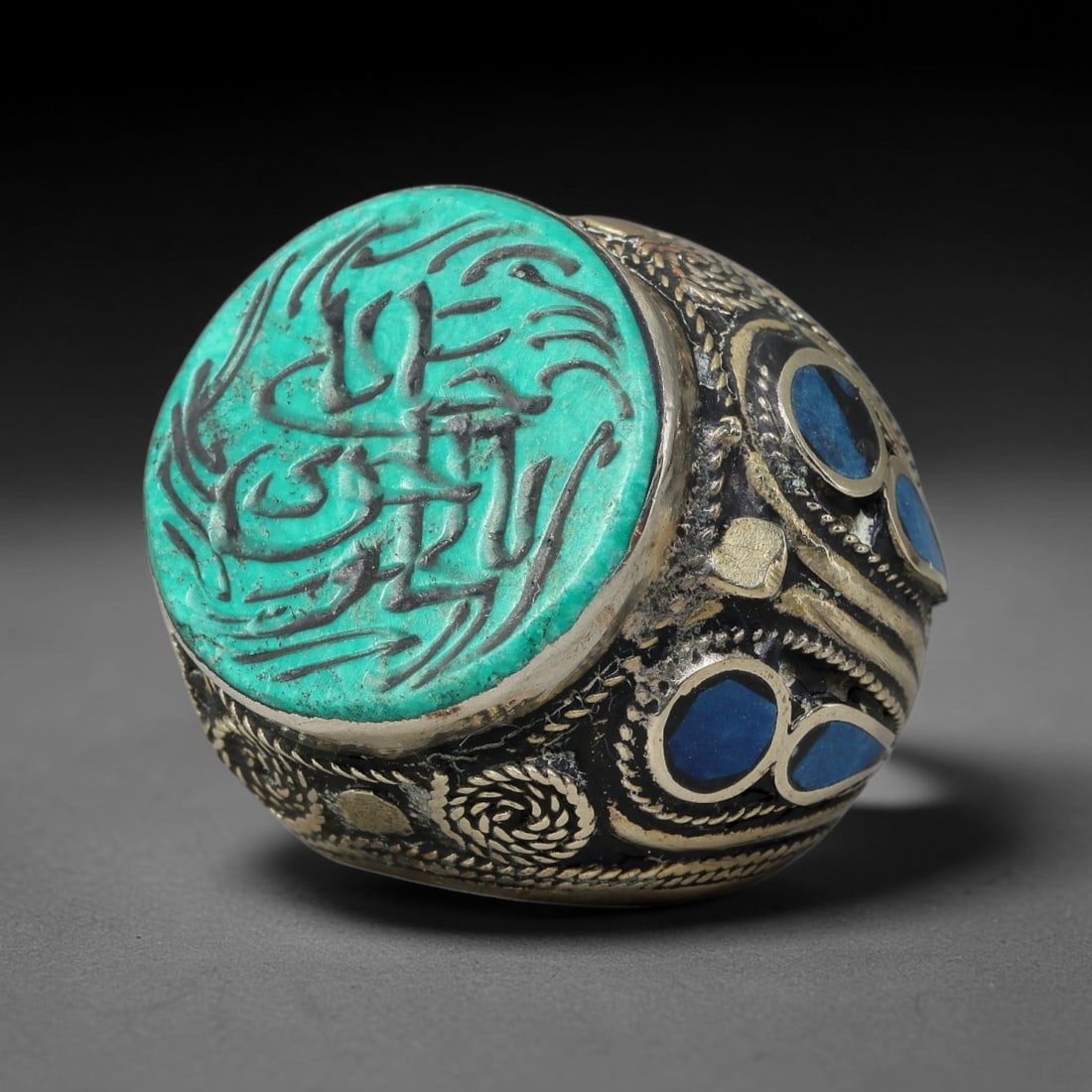 Vintage Islamic Handcrafted Silver Plated Calligraphic Talisman Statement Ring, 17BX: This vintage hand-wrought Islamic statement ring features a central engraved panel bearing traditional calligraphic detailing, set within an ornate silver-plated metal band. The mounting is enriched w