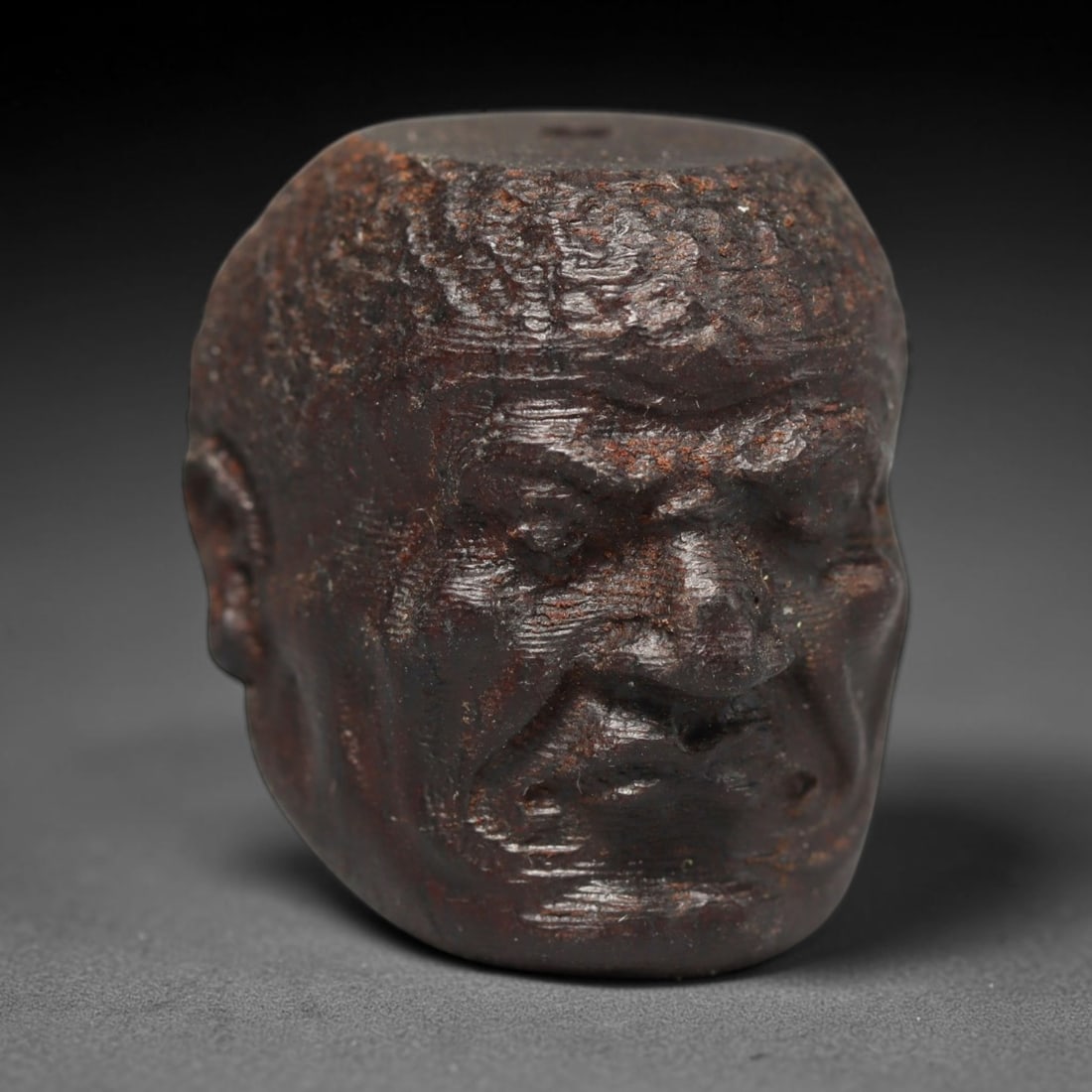 A Chinese Agar Wood Carved Head Art Bead, 36BX: Chinese agar wood head-form art bead measuring 22 x 20 mm. Detailed sculpted facial features cover the exterior surface, with a continuous central bore designed for stringing within beaded strands. Th
