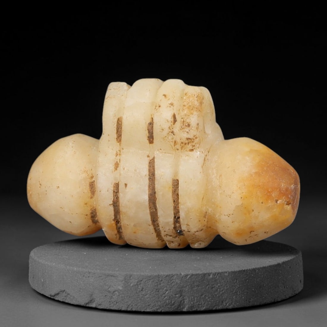Ancient Western Asiatic Banded Calcite Tiered Double Terminal Amulet (1000-600 BCE), 91AE: Hand-carved pale honey-toned calcite ritual pendant featuring symmetrical bulbous terminals flanking a central multi-tiered ribbed core. Deep vertical carved grooves run along the segmented central bo