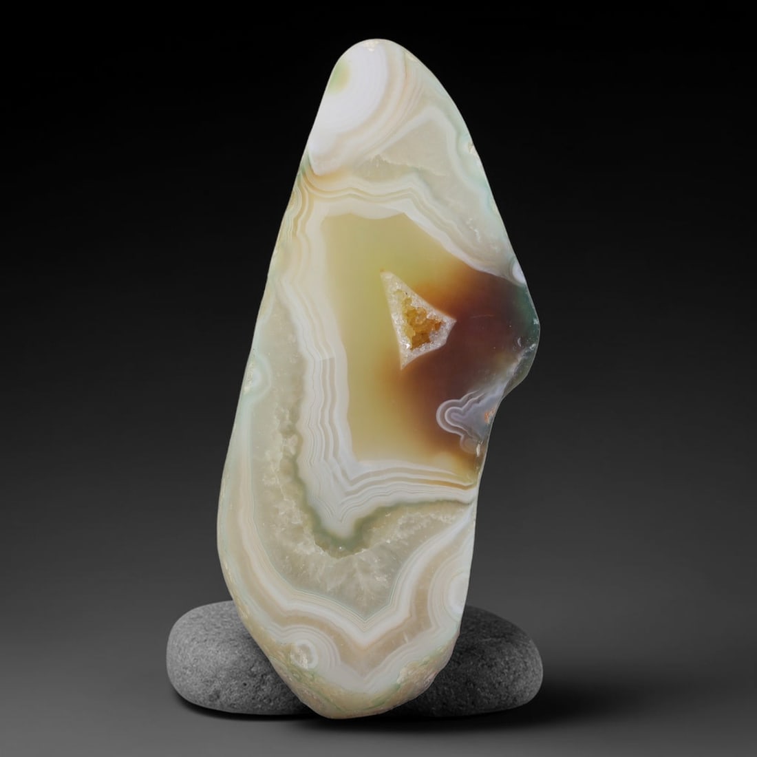 Natural Gobi Desert Banded Agate Slice with Central Druzy Pocket, 66AA: Polished natural Gobi desert agate slab measuring 6.2cm x 2.7cm, featuring delicate concentric layered banding in creamy white, soft sage green, honey amber and pale yellow tones. A distinct triangula