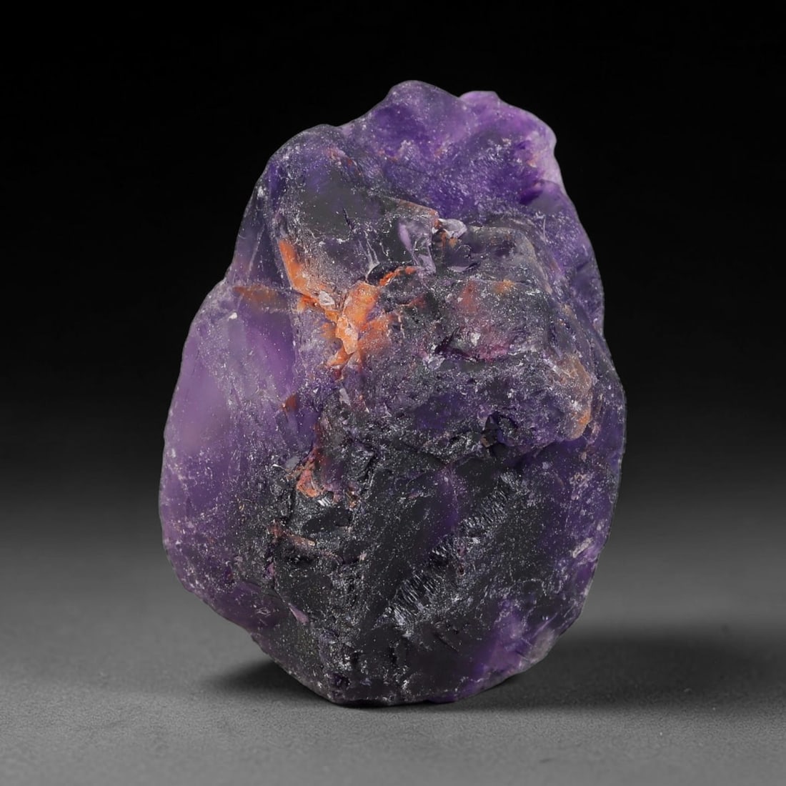 176ct Natural Chinese Deep Violet Purple Fluorite Rough, 12AT: This rugged fluorite rough boasts rich layered violet purple saturation blended with warm rust-colored mineral inclusions that streak its uneven raw surface, soft translucency lets light drift through