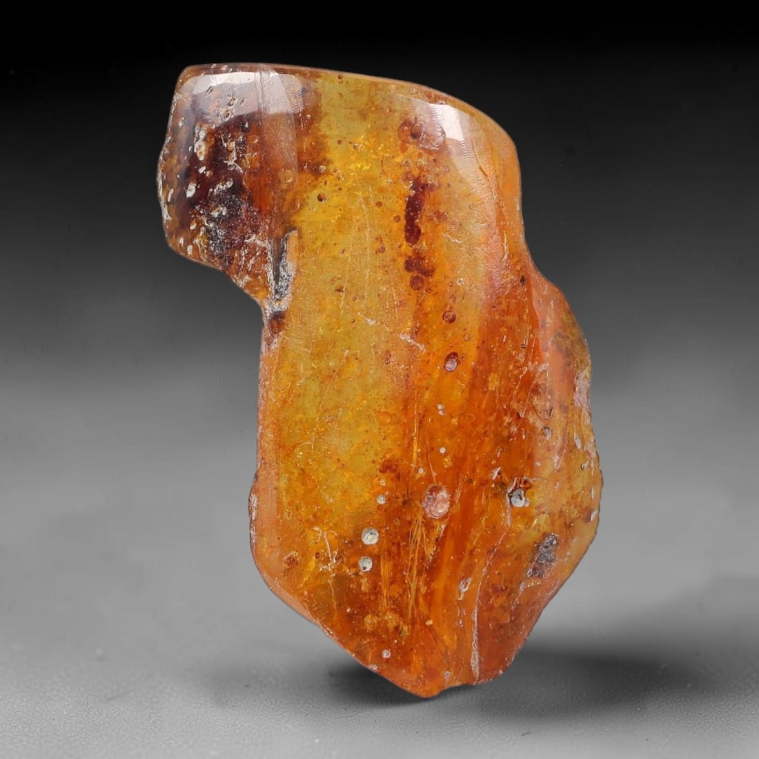 15.33ct Natural Baltic Polished Loose Freeform Amber Gemstone, 45EB: This smoothly polished freeform amber piece carries warm translucent organic clarity with fine natural fossil flecks and tiny mineral inclusions suspended throughout its 30x17mm flowing unstructured s