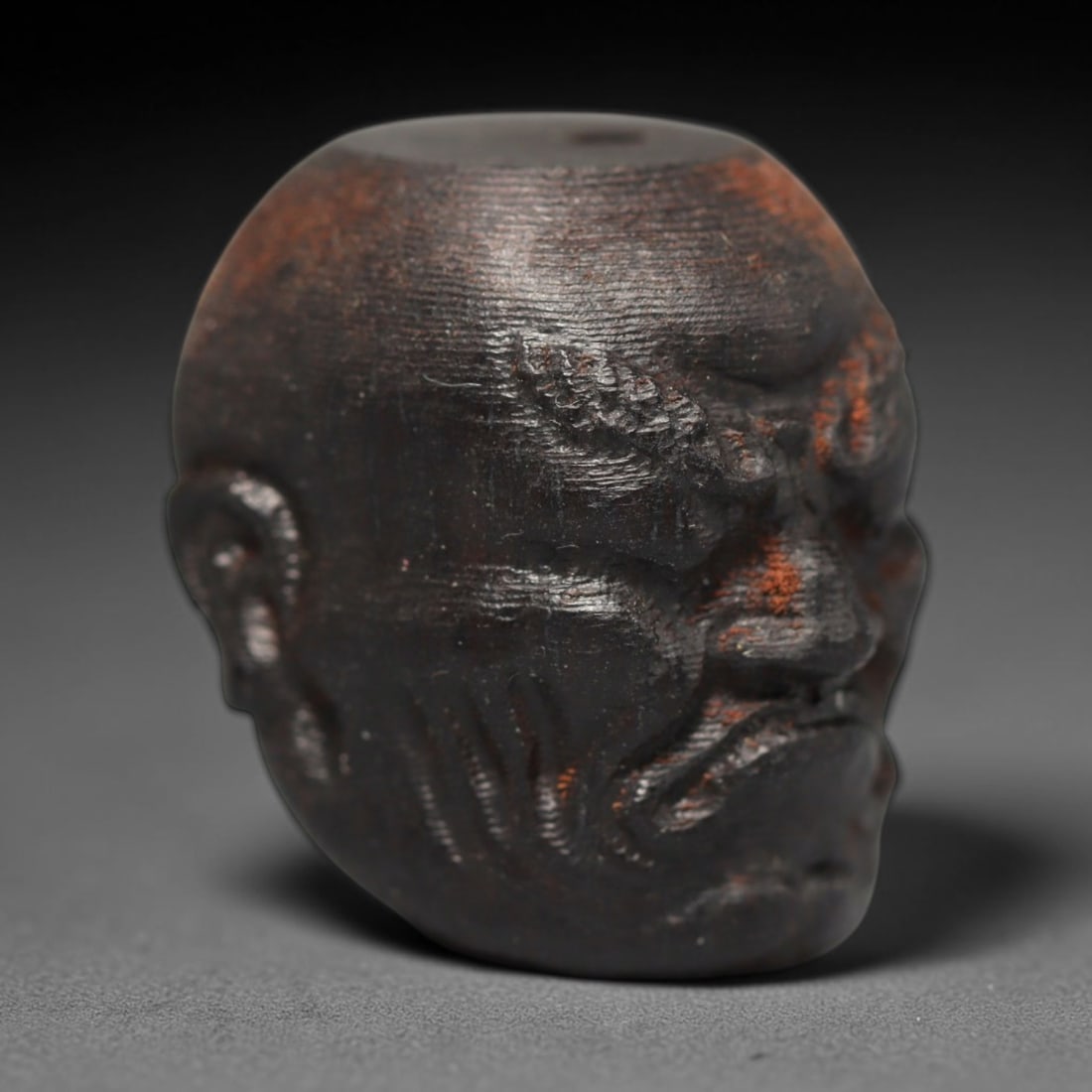 A Chinese Agar Wood Carved Head Art Bead, 25BX: Chinese agar wood head-form art bead measuring 22 x 20 mm. Detailed sculpted facial features cover the exterior surface, with a continuous central bore designed for stringing within beaded strands. Th