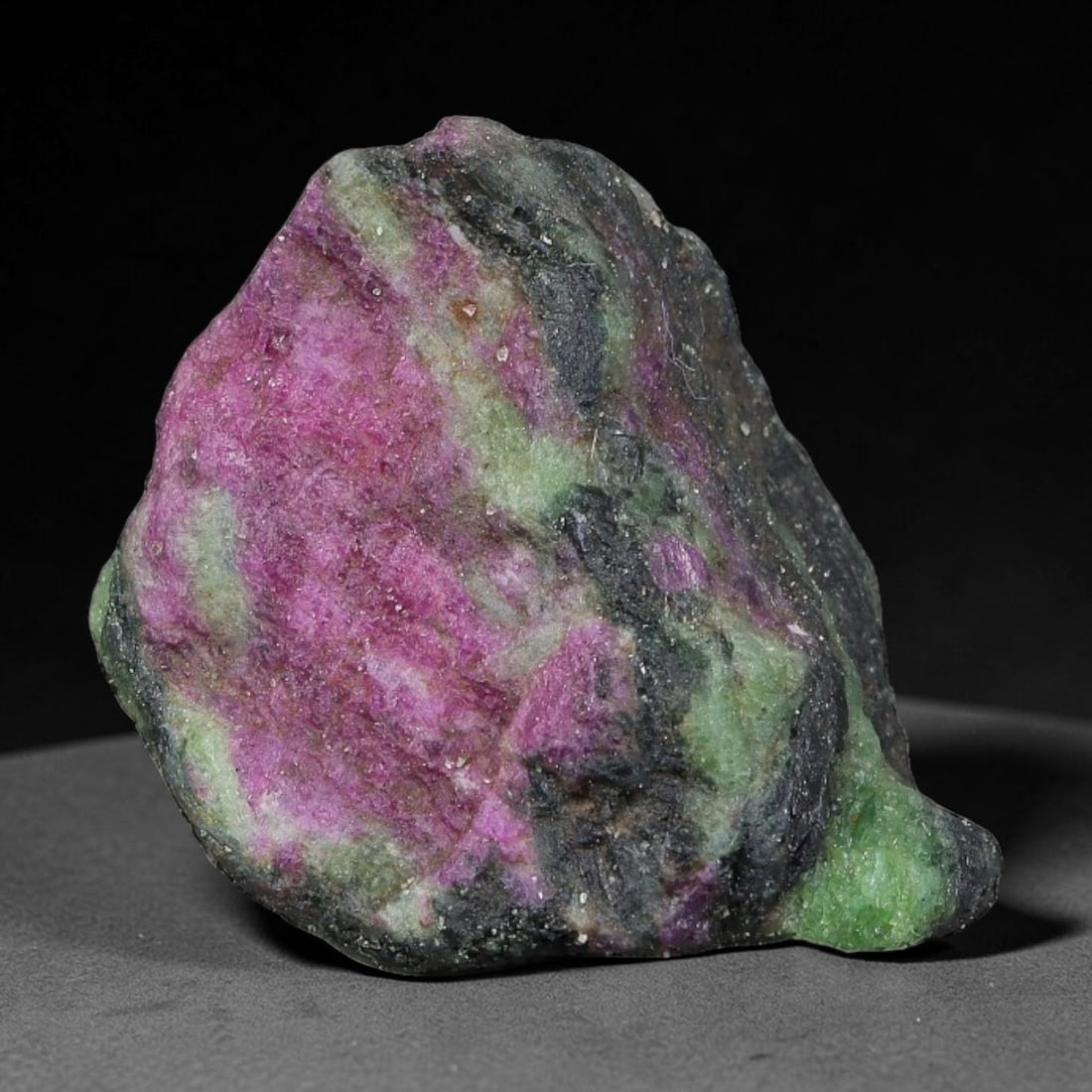 44ct Natural Tanzanian Ruby Zoisite Raw Rough Specimen Mineral Stone, 15FC: This unpolished mineral rough is natural ruby zoisite sourced from Tanzania, exhibiting distinct banded mineral segregation of vibrant green zoisite, magenta ruby crystals, and dark hornblende inclusi