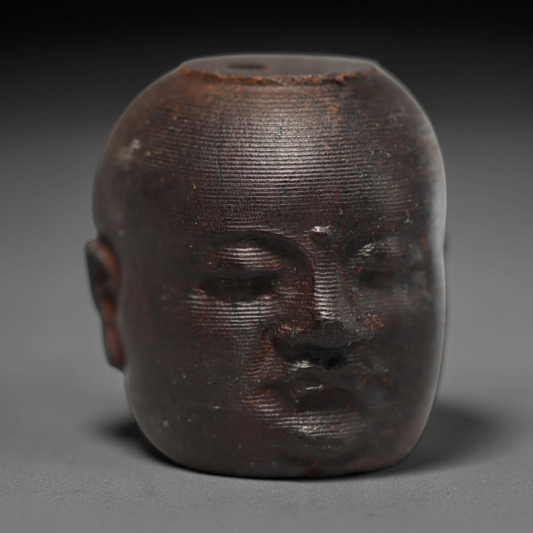 A Chinese Agar Wood Carved Head Art Bead, 21BX: Chinese agar wood head-form art bead measuring 22 x 20 mm. Detailed sculpted facial features cover the exterior surface, with a continuous central bore designed for stringing within beaded strands. Th