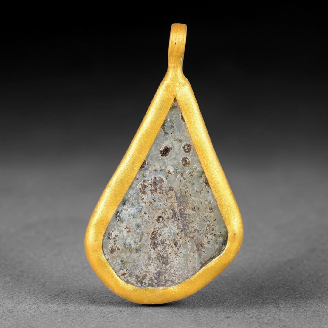 Ancient Roman Glass Slag in Modern Gilt-Edge Pendant, 59FY: This contemporary pendant is crafted from ancient Roman glass slag, featuring a fragmented, iridescent glass surface with weathered patina. The irregular form is bordered by a subtle gilt frame, added