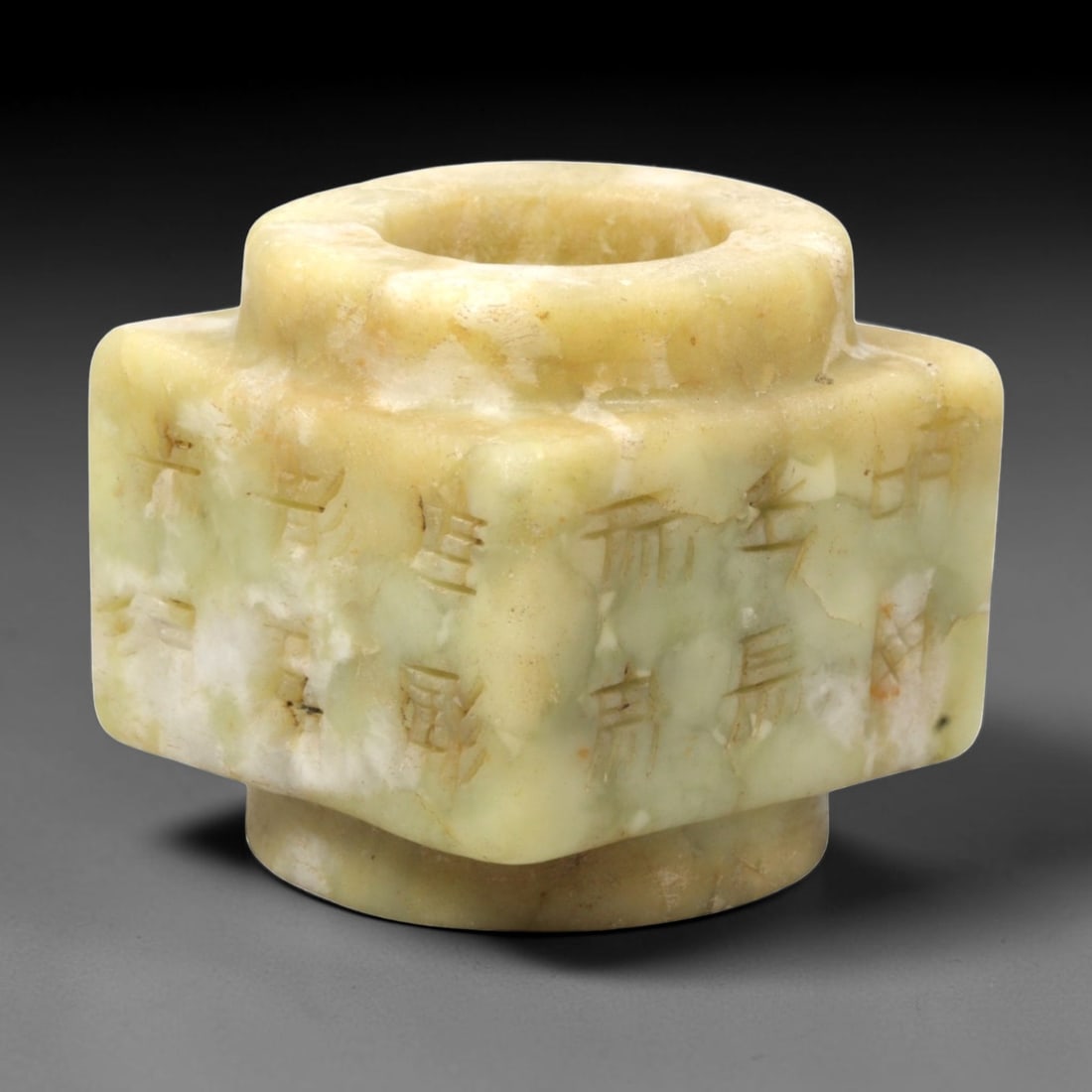 A Chinese Hetian Jade Cylindrical Ornament with Incised Characters, 93FH: Carved from mottled pale green and creamy-yellow Hetian jade, the object is formed as a stepped cylindrical vessel-like ornament with a thick-walled circular aperture and projecting shoulder. The exte