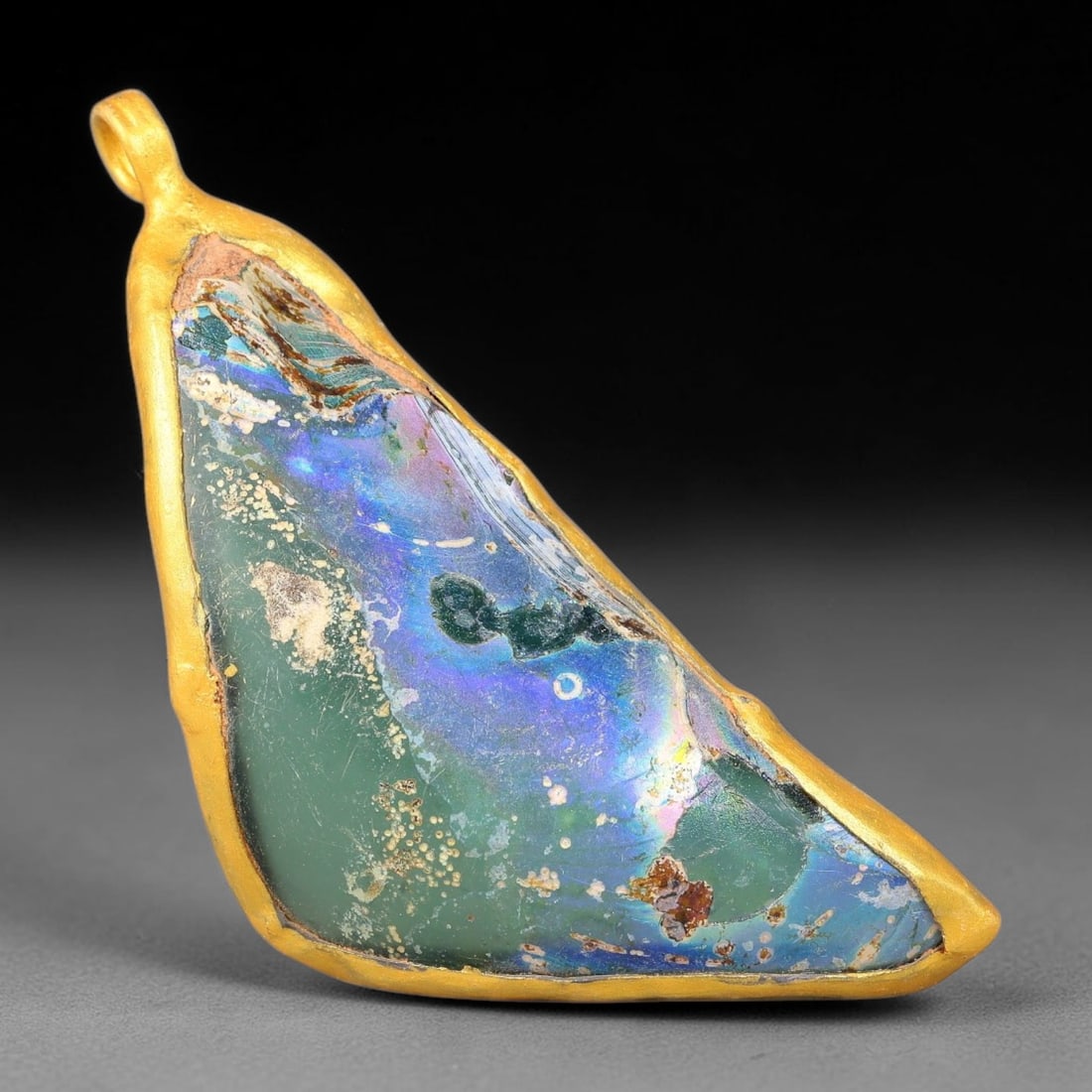 Ancient Roman Glass Slag in Modern Gilt-Edge Pendant, 45FY: This contemporary pendant is crafted from ancient Roman glass slag, featuring a fragmented, iridescent glass surface with weathered patina. The irregular form is bordered by a subtle gilt frame, added