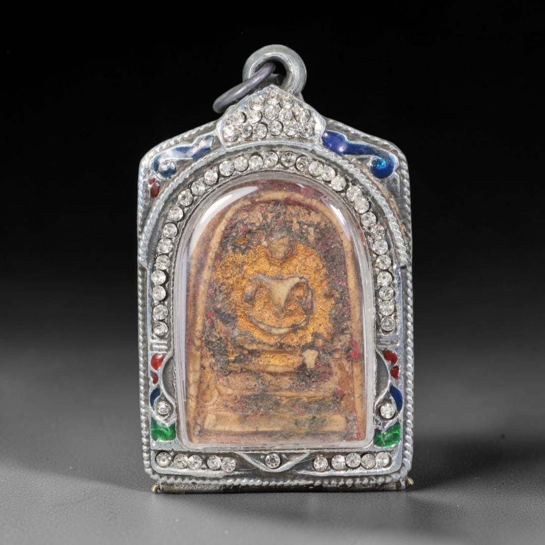 Thai Buddhist Folk Tradition Enclosed Amulet Pendant with Decorative Metal Casing, 38AH: This Thai sacred amulet is housed within an ornate hinged metal protective casing fitted with a top loop for wear as a pendant. The casing features intricate embossed surface detailing and a continuou