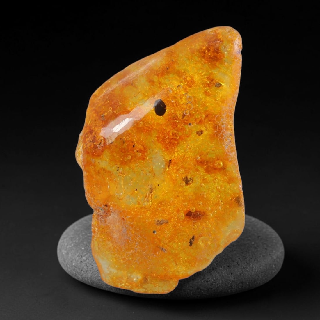12.57ct Natural Baltic Polished Loose Freeform Amber Gemstone, 38AT: This smoothly polished freeform amber piece carries warm translucent organic clarity with fine natural fossil flecks and tiny mineral inclusions suspended throughout its 33x19mm flowing unstructured s