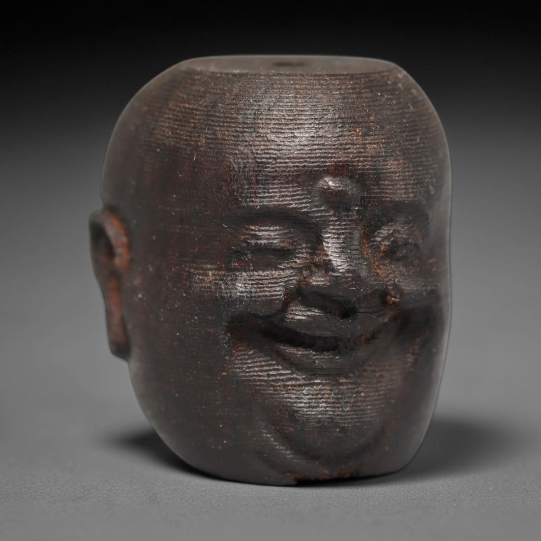 A Chinese Agar Wood Carved Head Art Bead, 24BX: Chinese agar wood head-form art bead measuring 22 x 20 mm. Detailed sculpted facial features cover the exterior surface, with a continuous central bore designed for stringing within beaded strands. Th