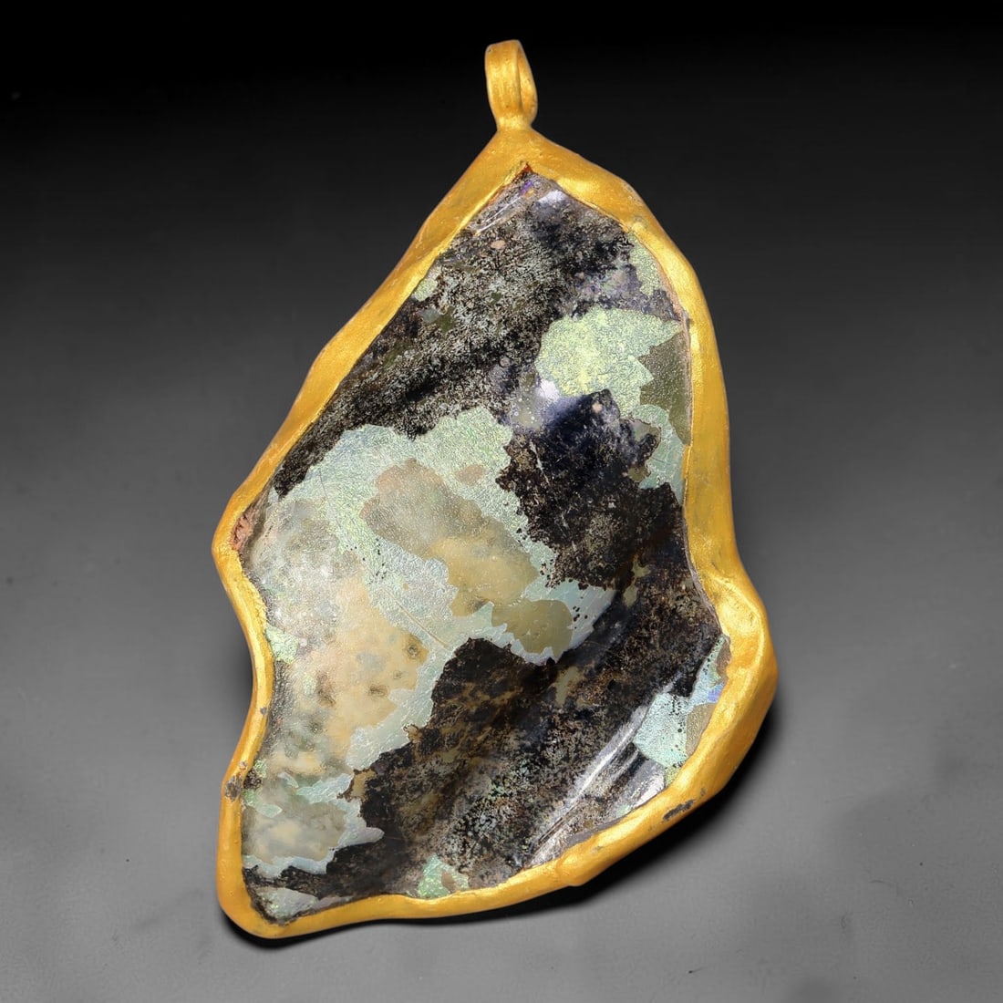 Ancient Roman Glass Slag in Modern Gilt-Edge Pendant, 48FY: This contemporary pendant is crafted from ancient Roman glass slag, featuring a fragmented, iridescent glass surface with weathered patina. The irregular form is bordered by a subtle gilt frame, added