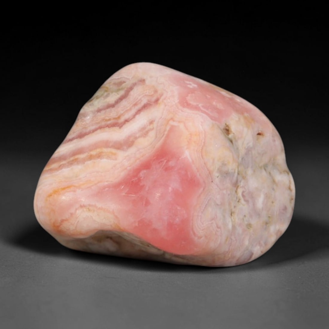 75ct Natural Argentine Rhodochrosite Tumbled Banded Rough Specimen, 1FD: This smooth rounded rough specimen is natural banded rhodochrosite sourced from Argentina's Capillitas mining district, displaying characteristic layered concentric banding of soft blush pink, creamy 