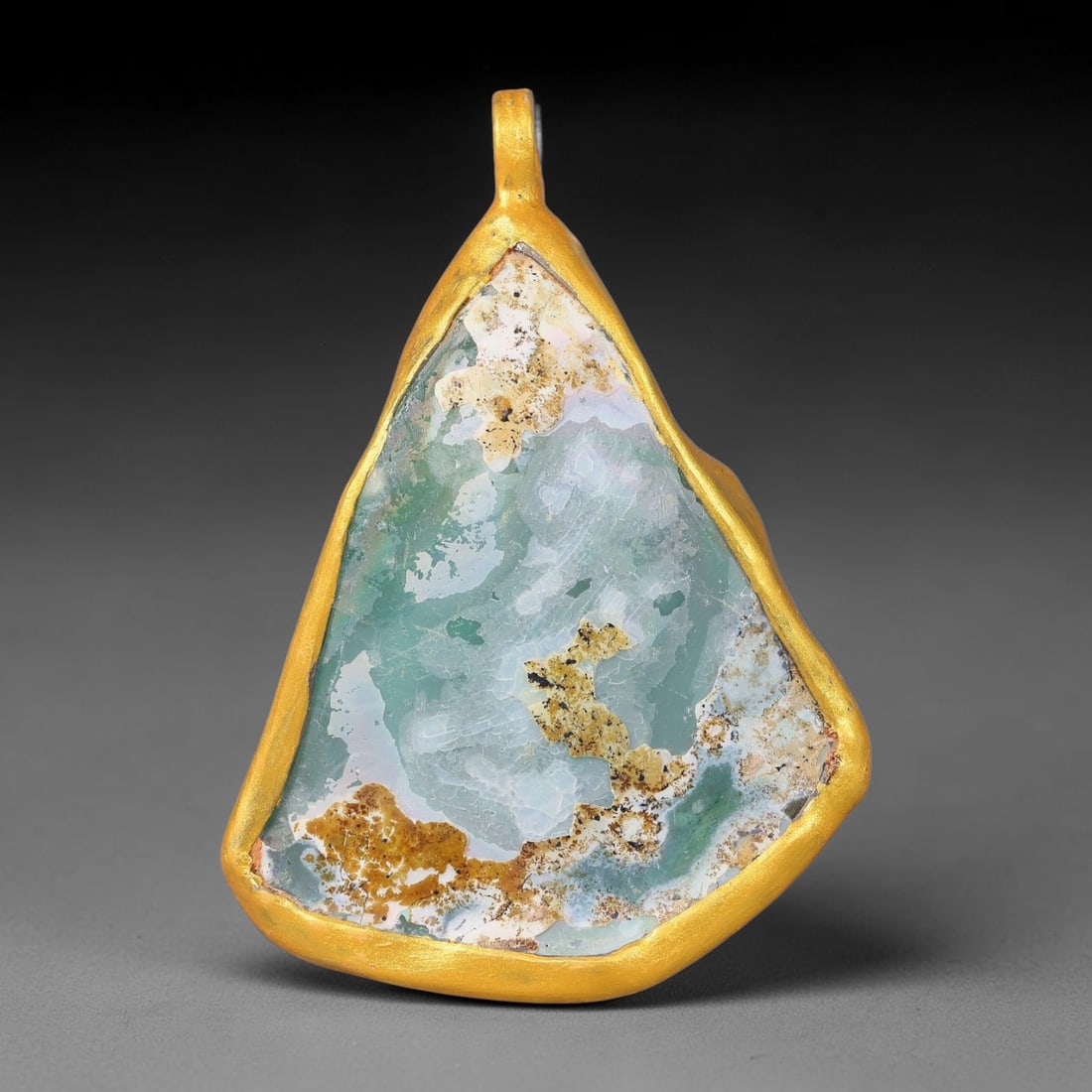 Ancient Roman Glass Slag in Modern Gilt-Edge Pendant, 44FY: This contemporary pendant is crafted from ancient Roman glass slag, featuring a fragmented, iridescent glass surface with weathered patina. The irregular form is bordered by a subtle gilt frame, added
