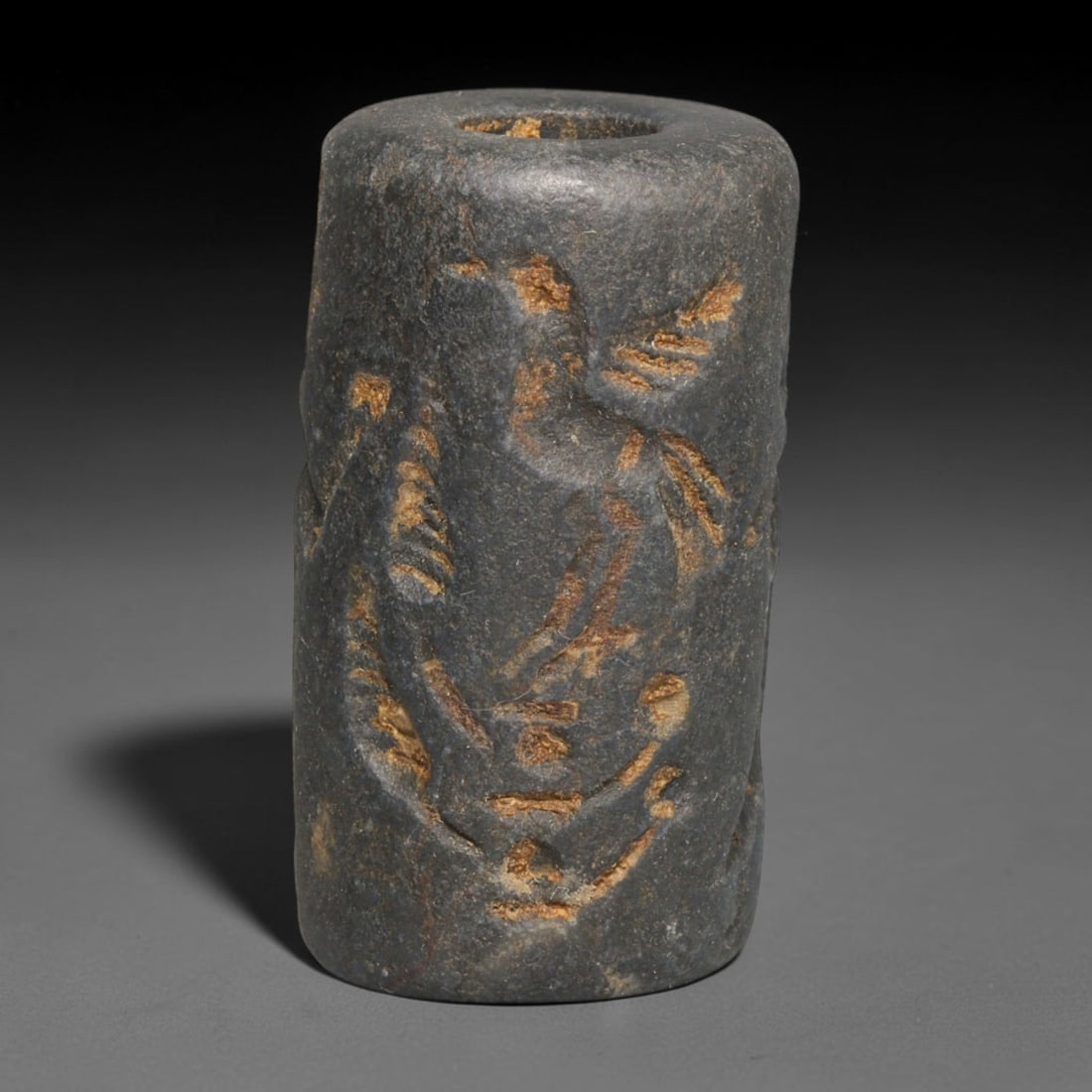 Ancient Sasanian Persian Dark Stone Cylinder Seal (c.224-651 CE), 58EC: This dark stone cylinder seal originates from the Sasanian Persian Empire (c.224-651 CE). The exterior features deeply incised two-sided intaglio imagery, including robed human figures and avian motif