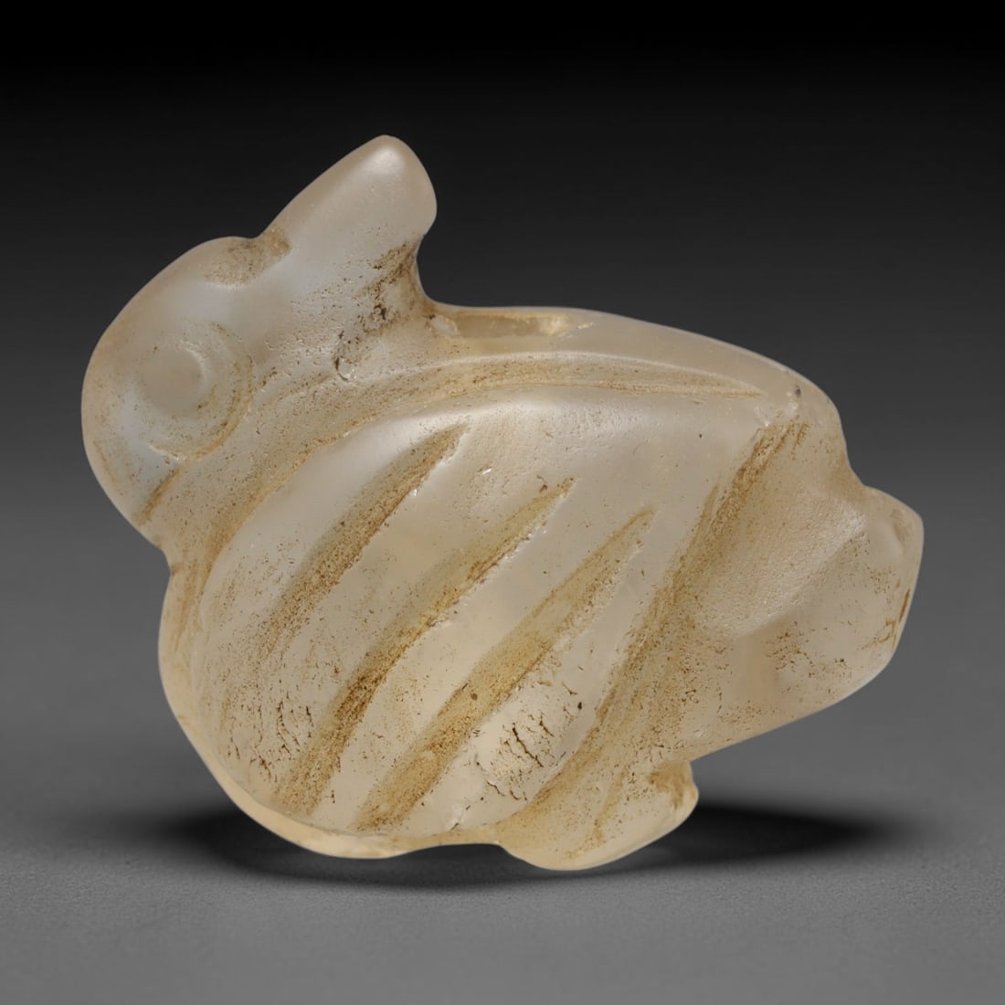 Ancient Medieval Early Islamic Period Rock Crystal Zoomorphic Amulet (c.7th-11th Century CE), 100EC: This miniature pierced talisman is carved from natural rock crystal, rendered in zoomorphic form. Subtle incised detailing defines the body, and a horizontal perforation allows suspension for wear. Ea