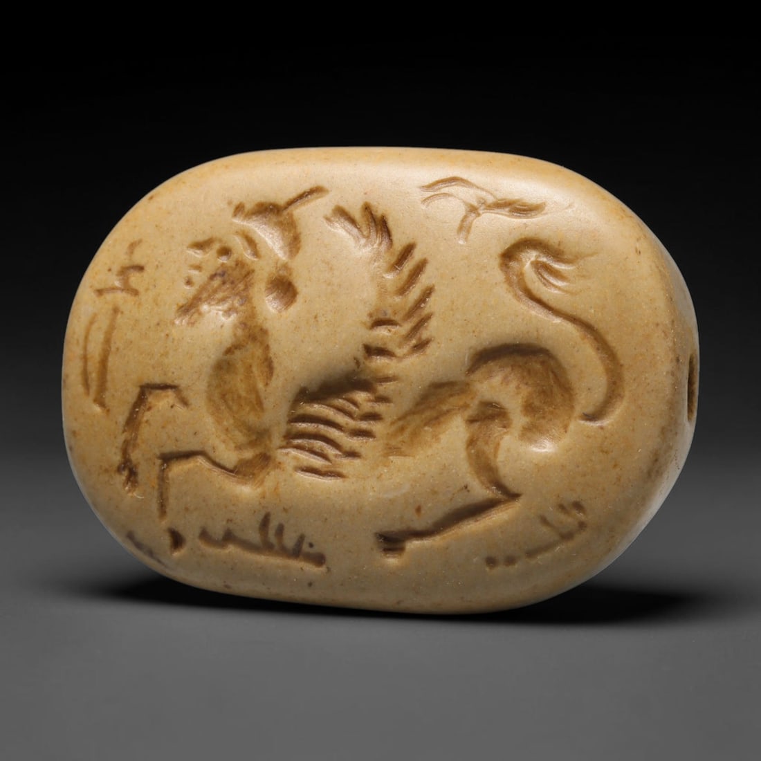 Ancient Sasanian Pale Stone Lamassu Intaglio Bead (224-651 CE), 64EC: This pierced oval pale stone intaglio bead originates from the Sasanian Persian Empire. The carved surface depicts a lamassu, the revered winged guardian beast inherited from ancient Mesopotamian icon