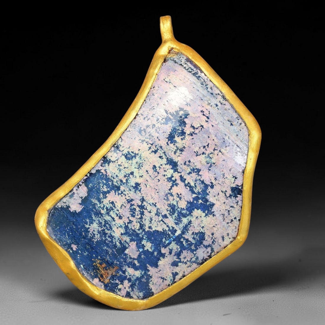 Ancient Roman Glass Slag in Modern Gilt-Edge Pendant, 46FY: This contemporary pendant is crafted from ancient Roman glass slag, featuring a fragmented, iridescent glass surface with weathered patina. The irregular form is bordered by a subtle gilt frame, added