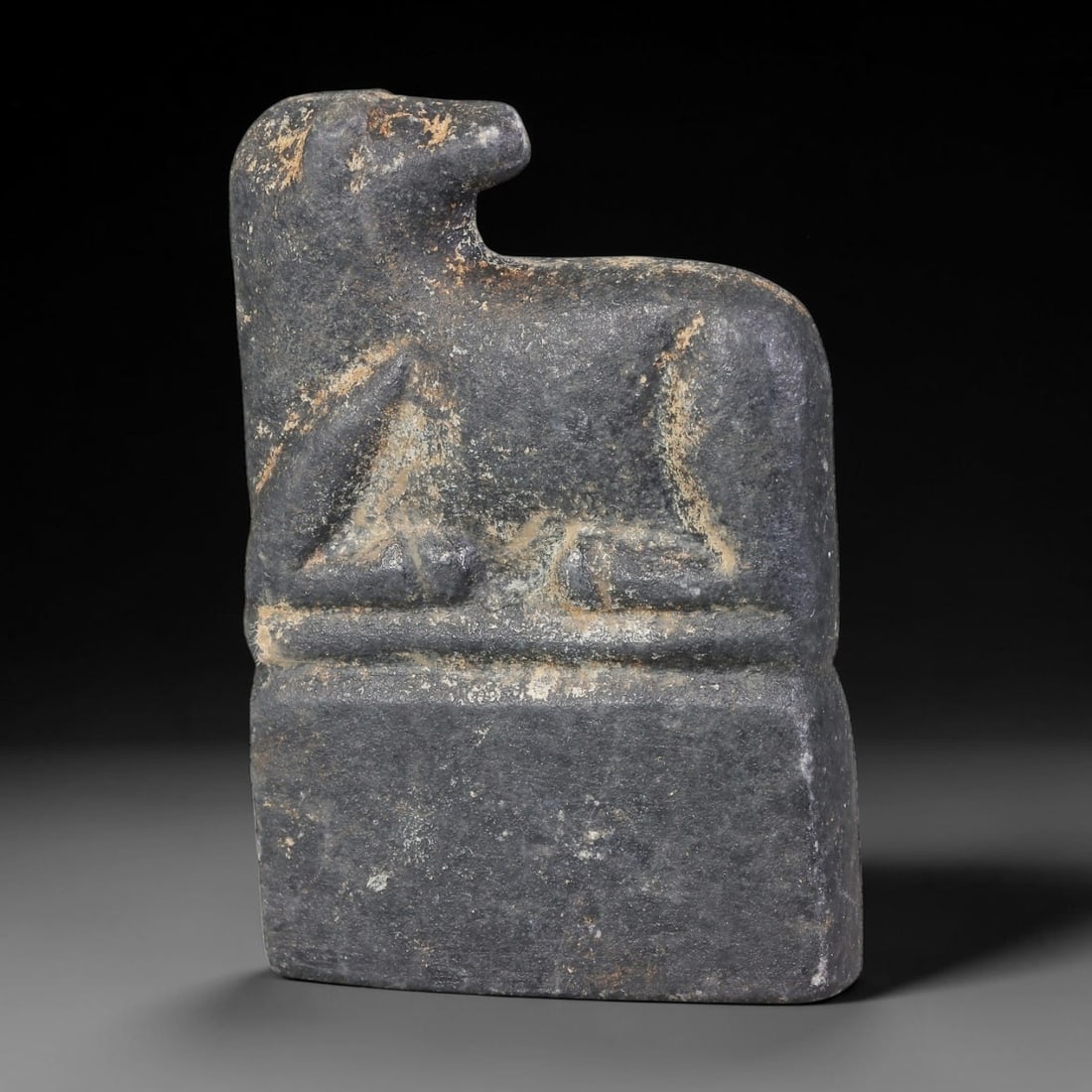 Ancient Near Eastern Dark Slate Recumbent Equine Zoomorphic Stela Amulet (1000-600 BCE), 46AB: Hand-carved dark grey slate miniature cult plaque featuring a stylized recumbent equine figure atop a solid rectangular plinth. Minimal incised lines define the animal's head, limbs and torso, with sc