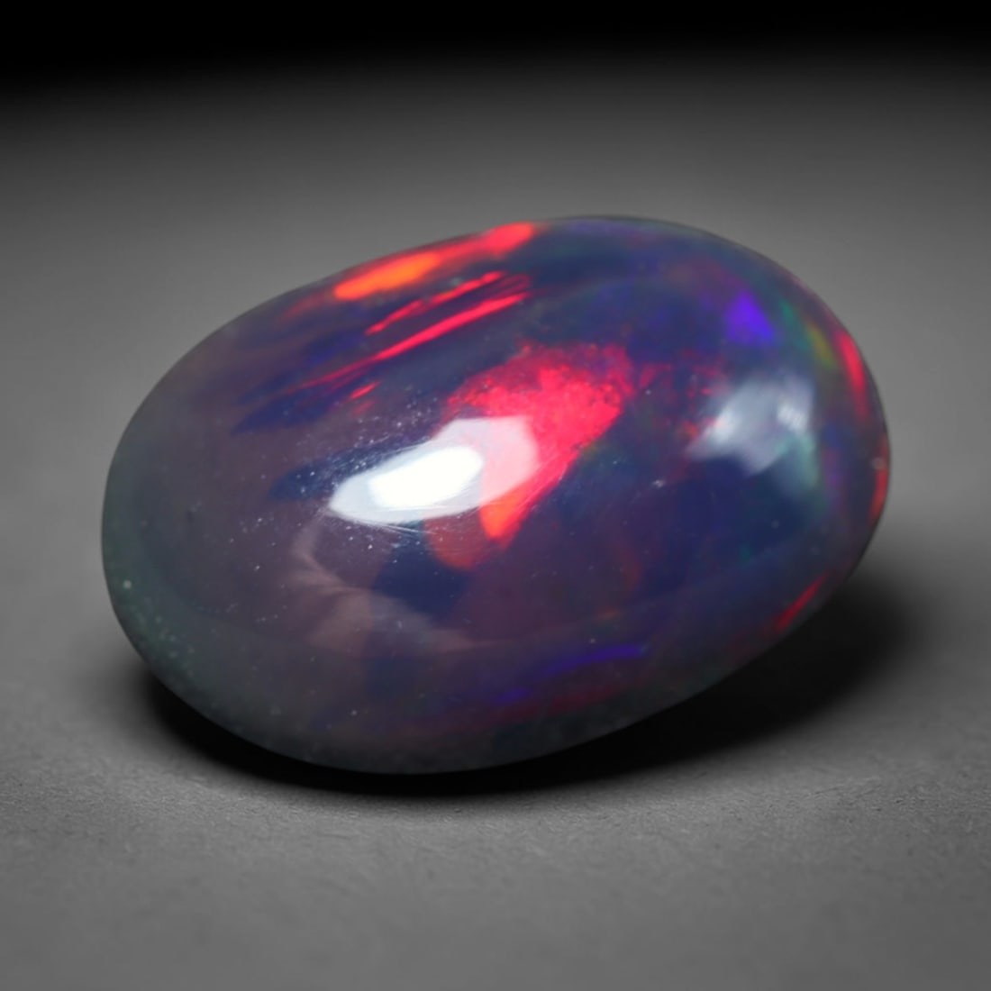 2.32ct Natural Ethiopian Welo Black Smoked Opal Cabochon Loose Gemstone, 50BY: This fully polished Ethiopian Welo opal features a dark smoked base with vivid, sweeping play-of-color shifting across its glossy dome surface, measured at 12x8x5mm. The black smoke treatment deepens 