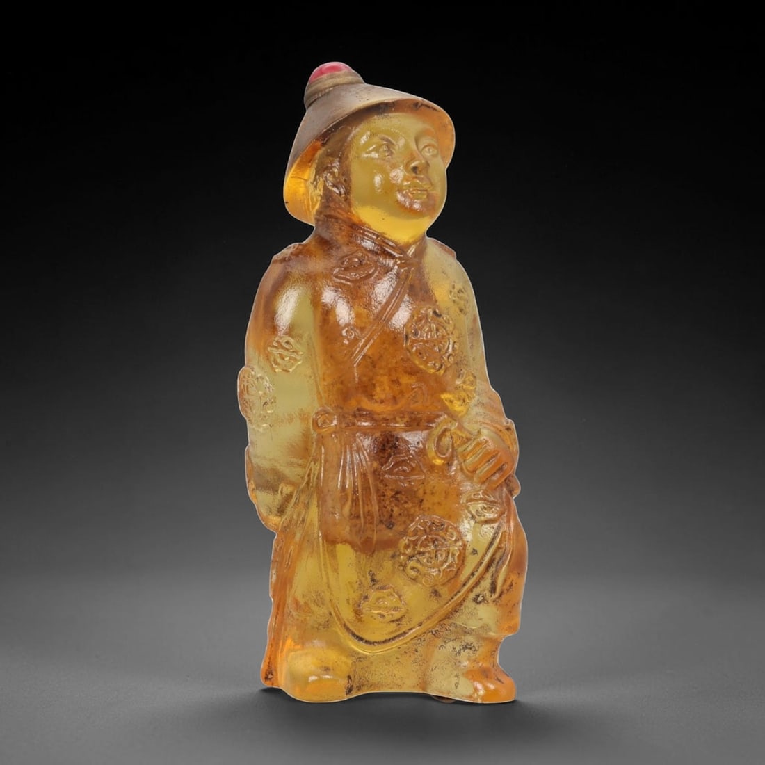 A Chinese Molded Glass Figural Snuff Bottle, 20th Century, 72FG: The snuff bottle is molded in the form of a standing male figure, likely representing a traditional attendant or official, dressed in long robes and a brimmed hat. The glass is of warm amber-golden to