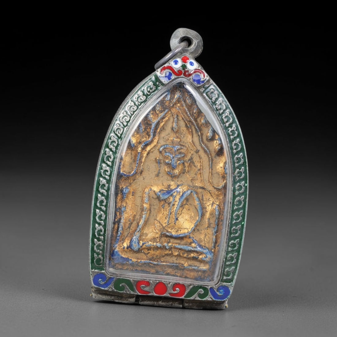 Thai Buddhist Folk Tradition Enclosed Amulet Pendant with Decorative Metal Casing, 16AH: This Thai sacred amulet is housed within an ornate hinged metal protective casing fitted with a top loop for wear as a pendant. The casing features intricate embossed surface detailing and a continuou