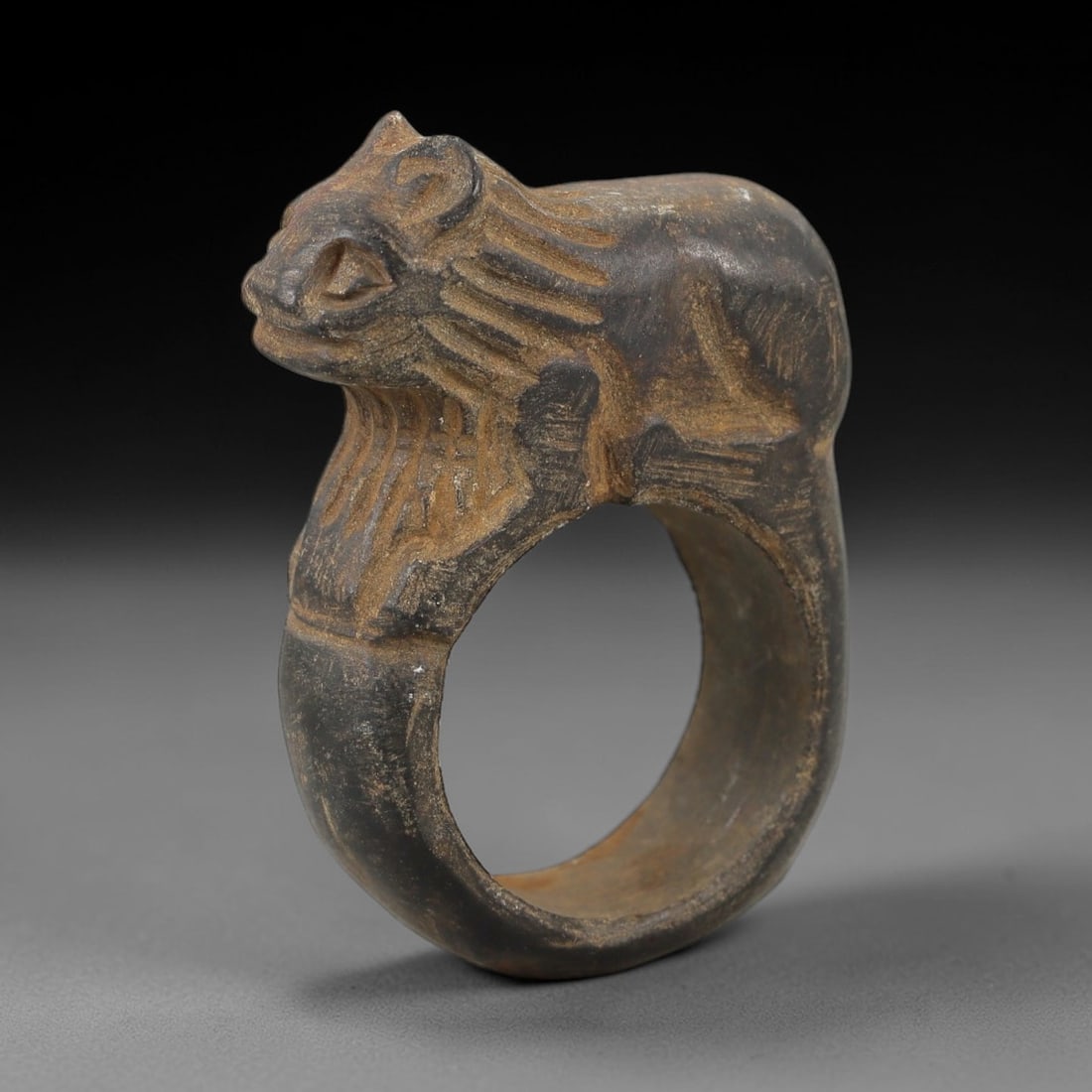 Ancient Parthian Carved Dark Stone Zoomorphic Figural Talisman Ring, 1FX: An ancient wearable ring carved from dark mineral stone, crafted within Parthian artistic traditions. The ring features a sculpted zoomorphic crest with carefully rendered textural detailing. Created 