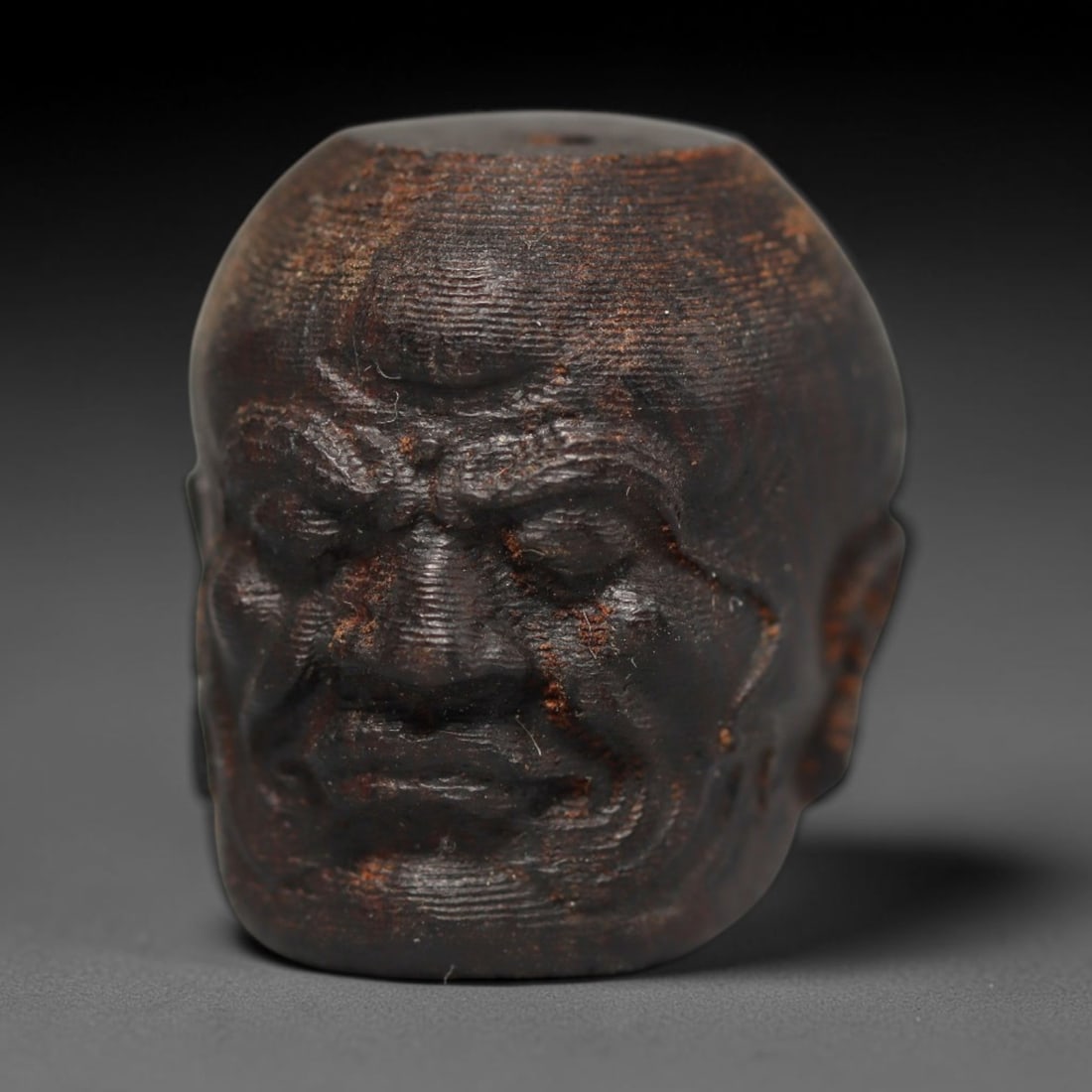 A Chinese Agar Wood Carved Head Art Bead, 34BX: Chinese agar wood head-form art bead measuring 22 x 20 mm. Detailed sculpted facial features cover the exterior surface, with a continuous central bore designed for stringing within beaded strands. Th