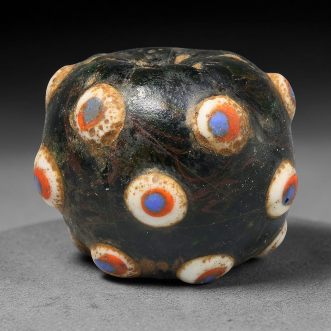 Ancient Medieval Islamic Eye Mosaic Glass Bead (800-1200 CE), 52ED: This antique mosaic glass bead originates from medieval Islamic glassmaking traditions, cherished for personal adornment and protective talismanic wear. The deep dark glass base is decorated with rais