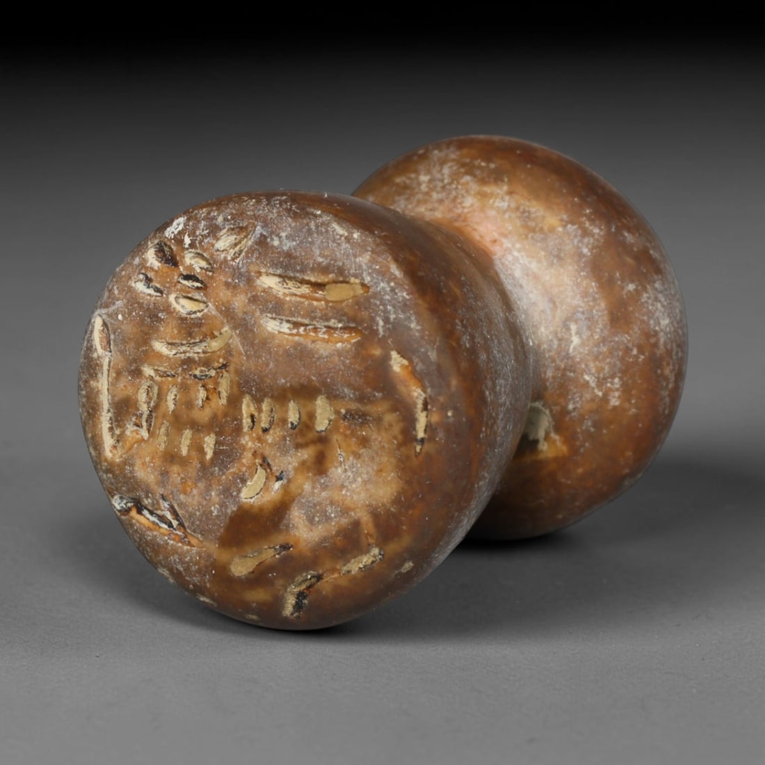 Ancient Sasanian Persian Double Domed Stamp Seal (c.224-651 CE), 19ED: This mottled brown stone double domed stamp seal originates from Ancient Sasanian Persian culture. The circular sealing face holds deeply incised symbolic motifs, crafted in characteristic regional ca