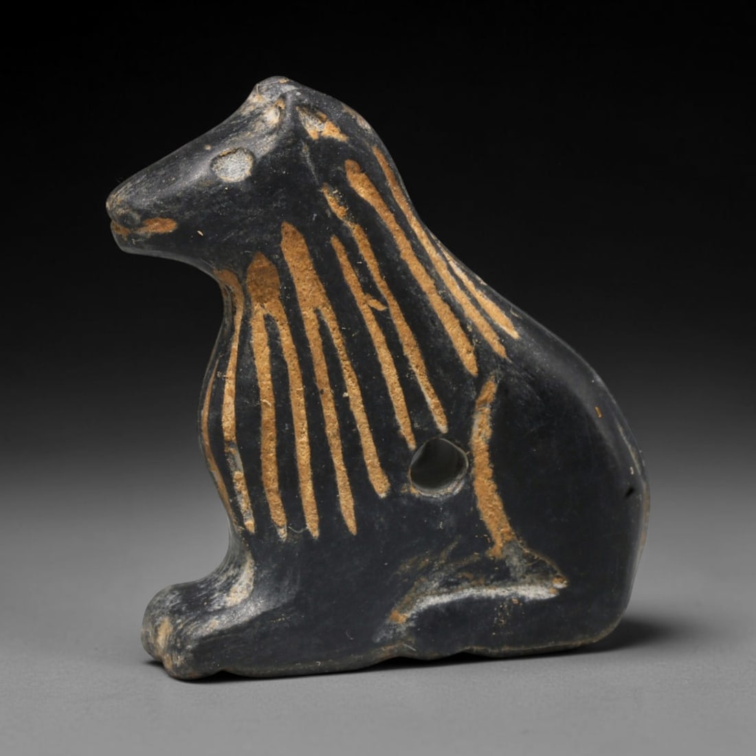Ancient Sasanian Persian Zoomorphic Amulet (c.224-651 CE), 23ED: This carved dark stone zoomorphic amulet originates from Ancient Sasanian Persian culture. The seated animal form is decorated with applied ochre detailing, and features a suspension hole for threadin