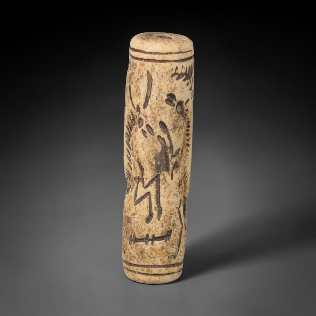 Ancient Mesopotamian Stone Cylinder Seal (c.2300-539 BCE), 72EF: This carved pale weathered stone cylinder seal originates from Ancient Mesopotamia. The cylindrical body features continuous incised imagery encircling the surface, framed by simple horizontal border 