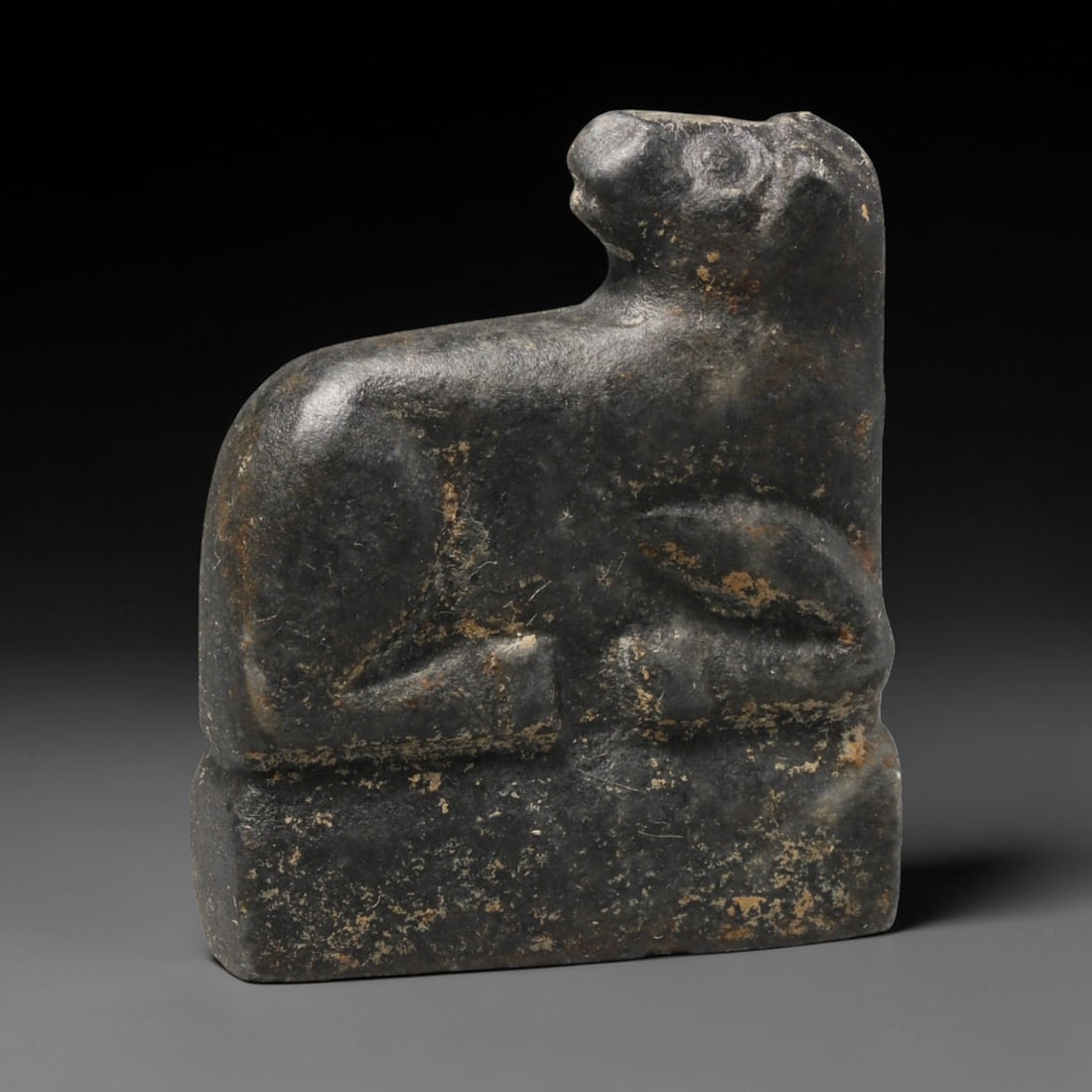 Ancient Bactrian Recumbent Feline Effigy (250 BCE-200 CE), 58ED: This carved dark stone recumbent feline effigy originates from Greco-Bactrian Culture, a historic Silk Road civilization blending Hellenistic and Central Asian artistic traditions. The animal rests up