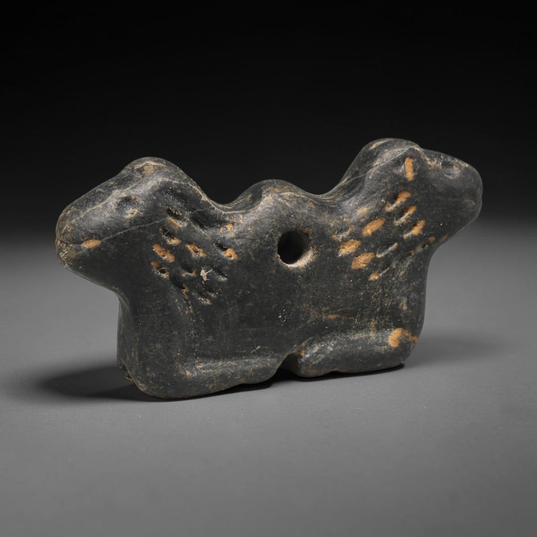 Ancient Sasanian Persian Zoomorphic Amulet (c.224-651 CE), 24ED: This carved dark stone zoomorphic amulet originates from Ancient Sasanian Persian culture. The compact resting animal form is decorated with simple incised detailing, and features a central suspension
