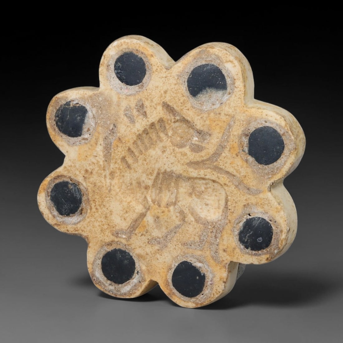 Ancient Neo-Hittite Floral Inlaid Limestone Stamp Seal (1200-800 BCE), 33EF: This eight-petalled floral stamp seal is carved from pale limestone, originating from Iron Age Neo-Hittite cultures of Northern Syria and Eastern Anatolia. Each petal socket holds a dark circular ston