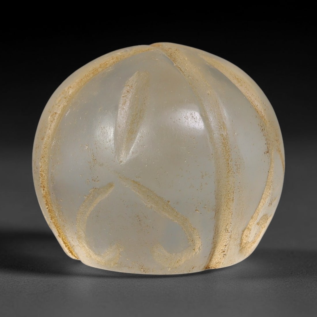 Ancient Mamluk Carved Glass Talisman Bead (13th-16th Centuries CE), 43EF: This bulbous carved talisman bead is crafted from translucent pale glass, dating to the Mamluk period. The exterior is segmented with raised ridging and decorated with lightly incised symbolic motifs,