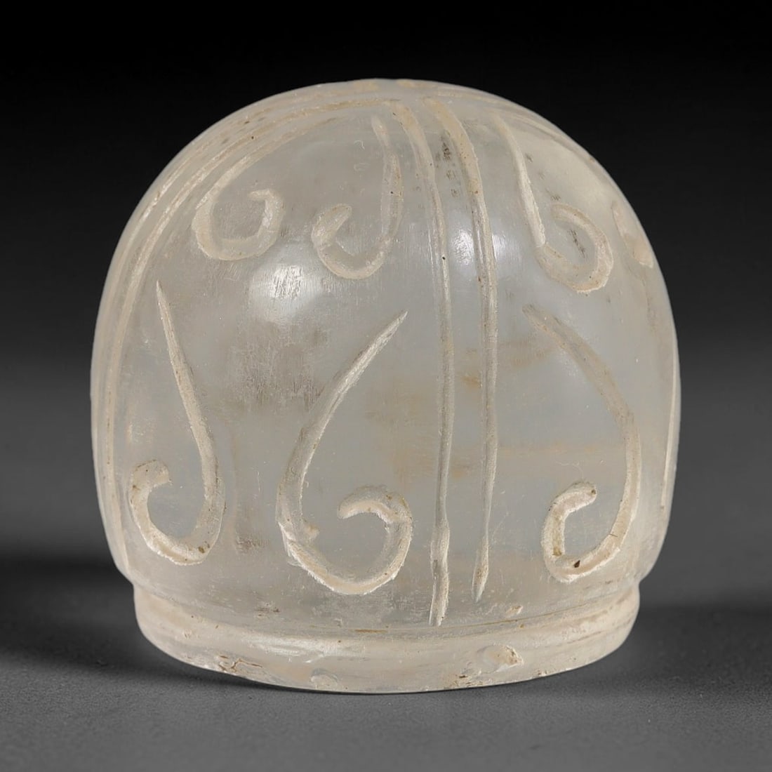 Ancient Mamluk Period Carved Clear Glass Talisman Ornament (1250-1517 CE), 44EF: This domed talisman ornament is crafted from translucent clear glass, dating to the Mamluk Sultanate. The exterior is decorated with deeply incised scrolling foliate motifs arranged in segmented verti