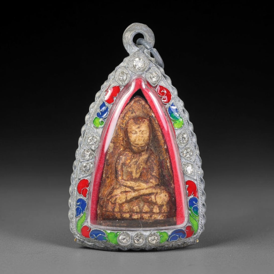 Thai Buddhist Folk Tradition Enclosed Amulet Pendant with Decorative Metal Casing, 27AH: This Thai sacred amulet is housed within an ornate hinged metal protective casing fitted with a top loop for wear as a pendant. The casing features intricate embossed surface detailing and a continuou