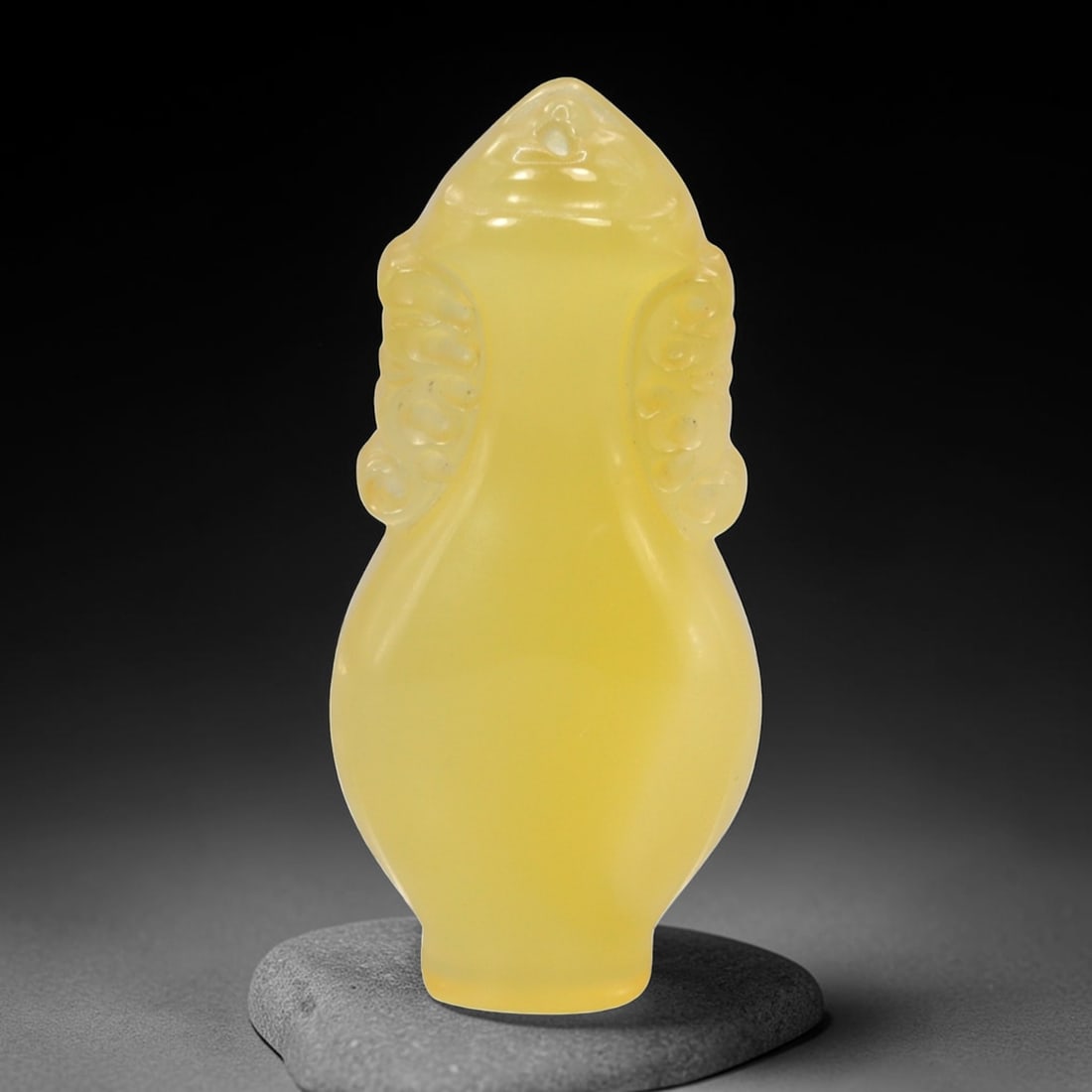 A Chinese Chalcedony or Yellow Jade Locket Pendant, 94FH: Carved from translucent yellow chalcedony with an even, softly diffused tone, the amulet is formed as a small locket-shaped vessel with a tapering neck and rounded body. The surface is smoothly polish