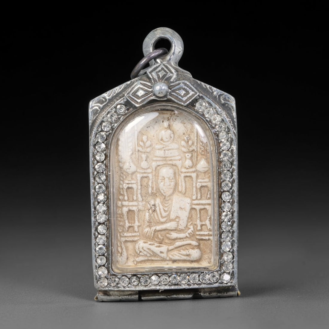 Thai Buddhist Folk Tradition Enclosed Amulet Pendant with Decorative Metal Casing, 34AH: This Thai sacred amulet is housed within an ornate hinged metal protective casing fitted with a top loop for wear as a pendant. The casing features intricate embossed surface detailing and a continuou