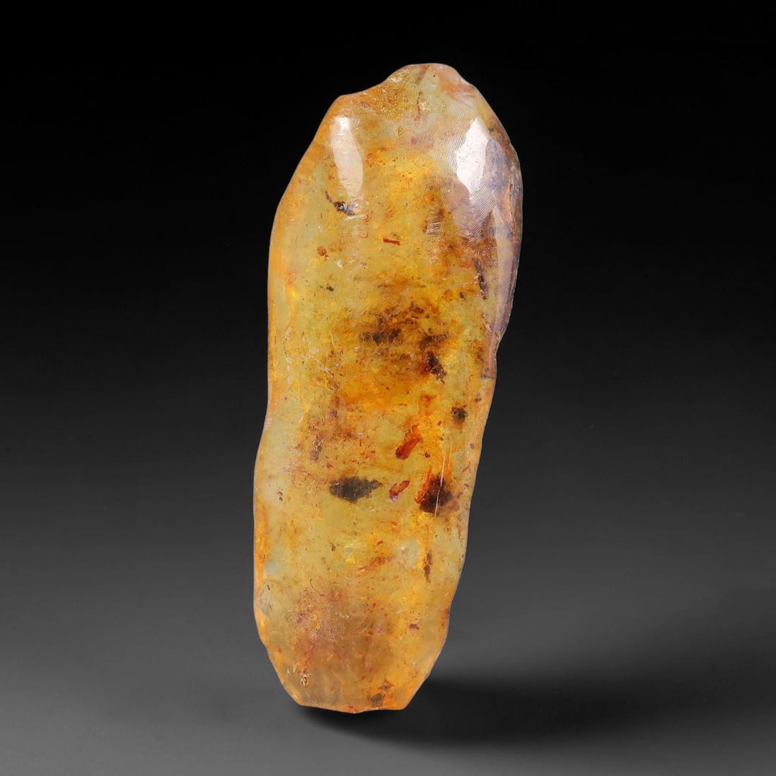 12.21ct Natural Baltic Polished Loose Freeform Amber Gemstone, 33EB: This smoothly polished freeform amber piece carries warm translucent organic clarity with fine natural fossil flecks and tiny mineral inclusions suspended throughout its 42x16mm flowing unstructured s