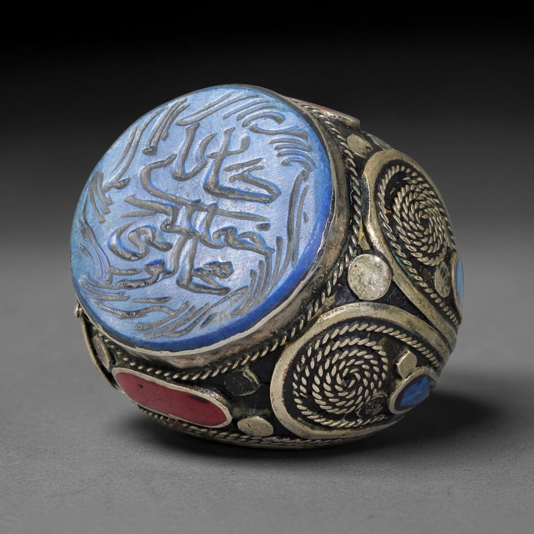Vintage Islamic Handcrafted Silver Plated Calligraphic Talisman Statement Ring, 1BX: This vintage hand-wrought Islamic statement ring features a central engraved panel bearing traditional calligraphic detailing, set within an ornate silver-plated metal band. The mounting is enriched w