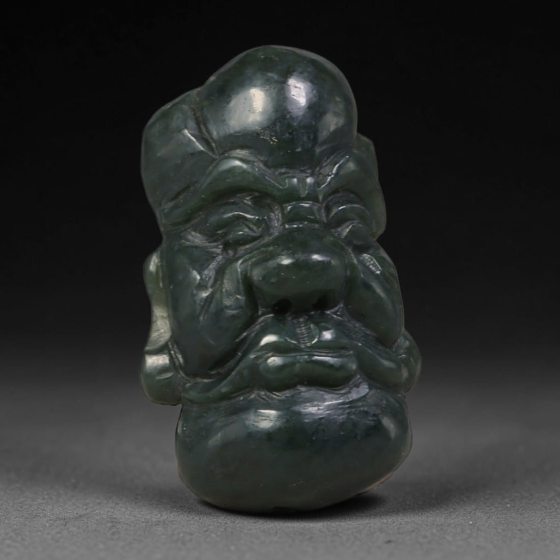 Natural Vintage Chinese Nephrite Jade Dark Green Arhat Head Carved Face Bead, 100AA: Hand-carved vintage Chinese strung bead crafted from natural vintage Chinese nephrite jade, measuring 3cm x 1.8cm. This solid barrel-shaped bead is intricately sculpted as a traditional Buddhist Arhat