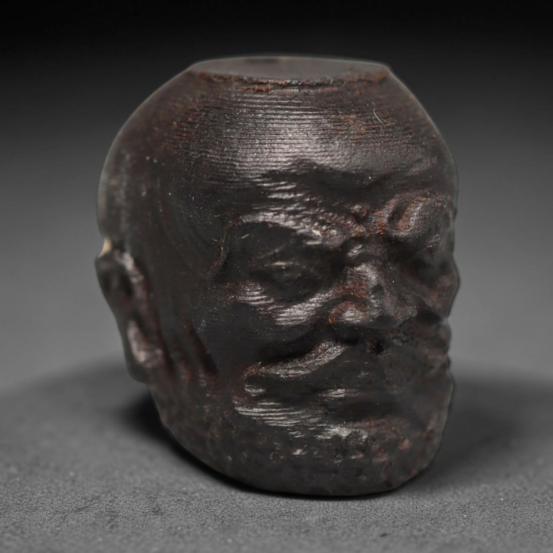 A Chinese Agar Wood Carved Head Art Bead, 32BX: Chinese agar wood head-form art bead measuring 22 x 20 mm. Detailed sculpted facial features cover the exterior surface, with a continuous central bore designed for stringing within beaded strands. Th