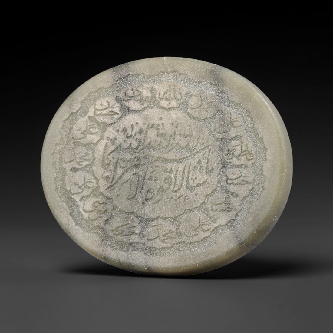 An Islamic Natural Green Stone Circular Script Engraved Talisman Tablet, 39FG: This polished green stone talisman tablet with elaborate concentric layered script engraving covering the central face, framed within a stylized petal-shaped inner border. Fine recessed engraved detai