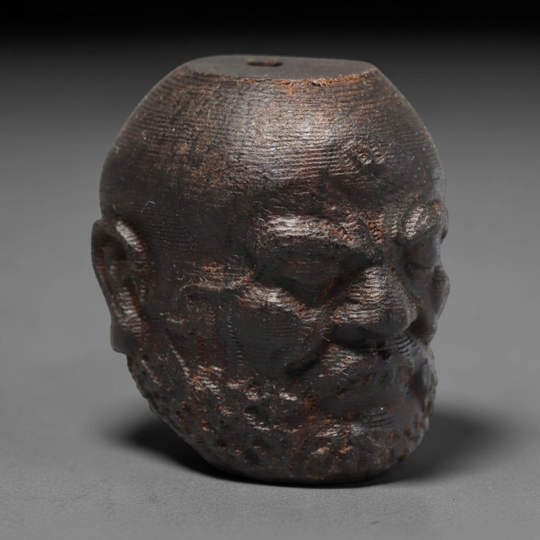 A Chinese Agar Wood Carved Head Art Bead, 26BX: Chinese agar wood head-form art bead measuring 22 x 20 mm. Detailed sculpted facial features cover the exterior surface, with a continuous central bore designed for stringing within beaded strands. Th