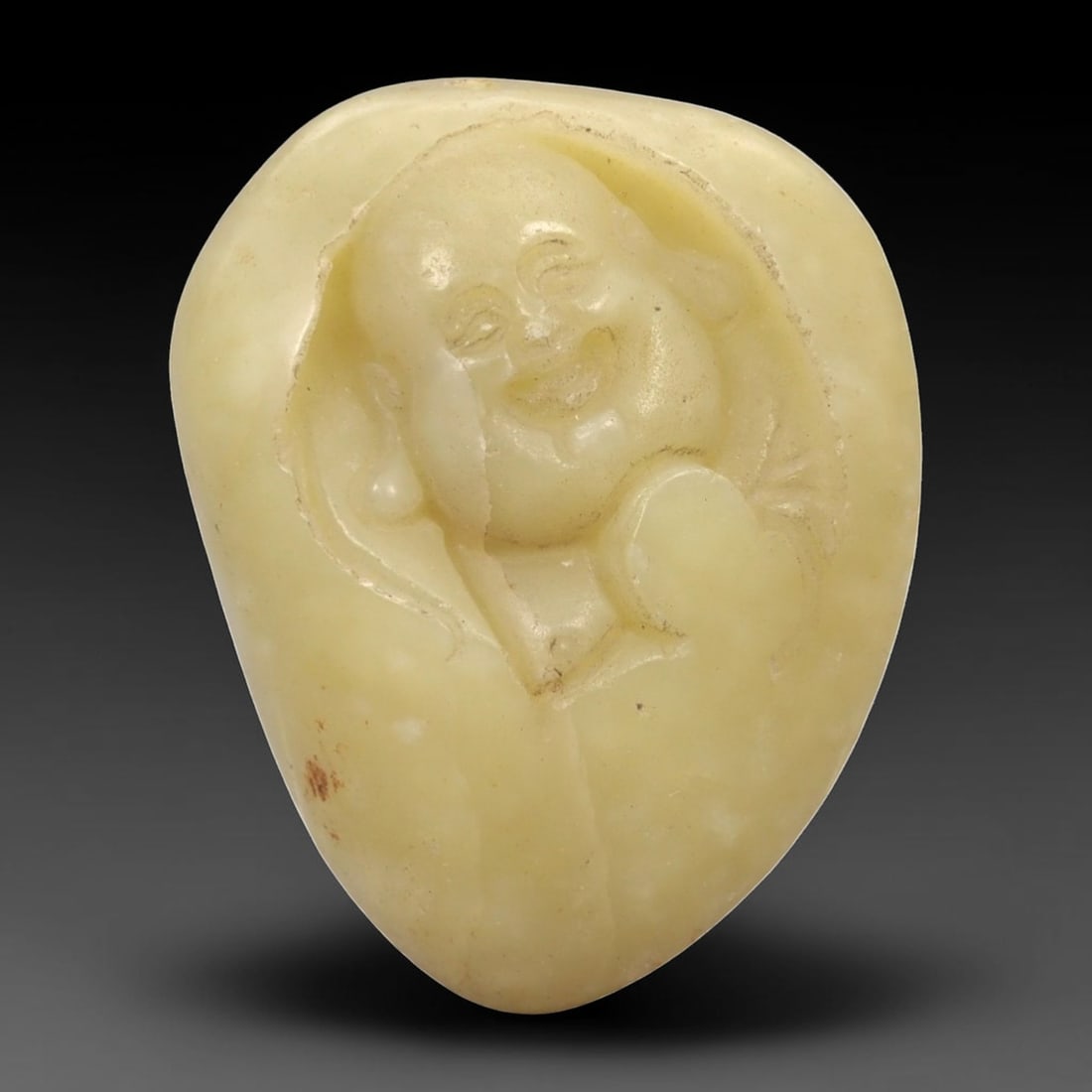 A Chinese Hetian Jade Pebble Carving of Budai, 20th Century, 92FH: Carved from a naturally rounded Hetian nephrite pebble of pale yellowish celadon tone, the carving depicts Budai shown in relief emerging from the natural contours of the stone. The figure is rendered